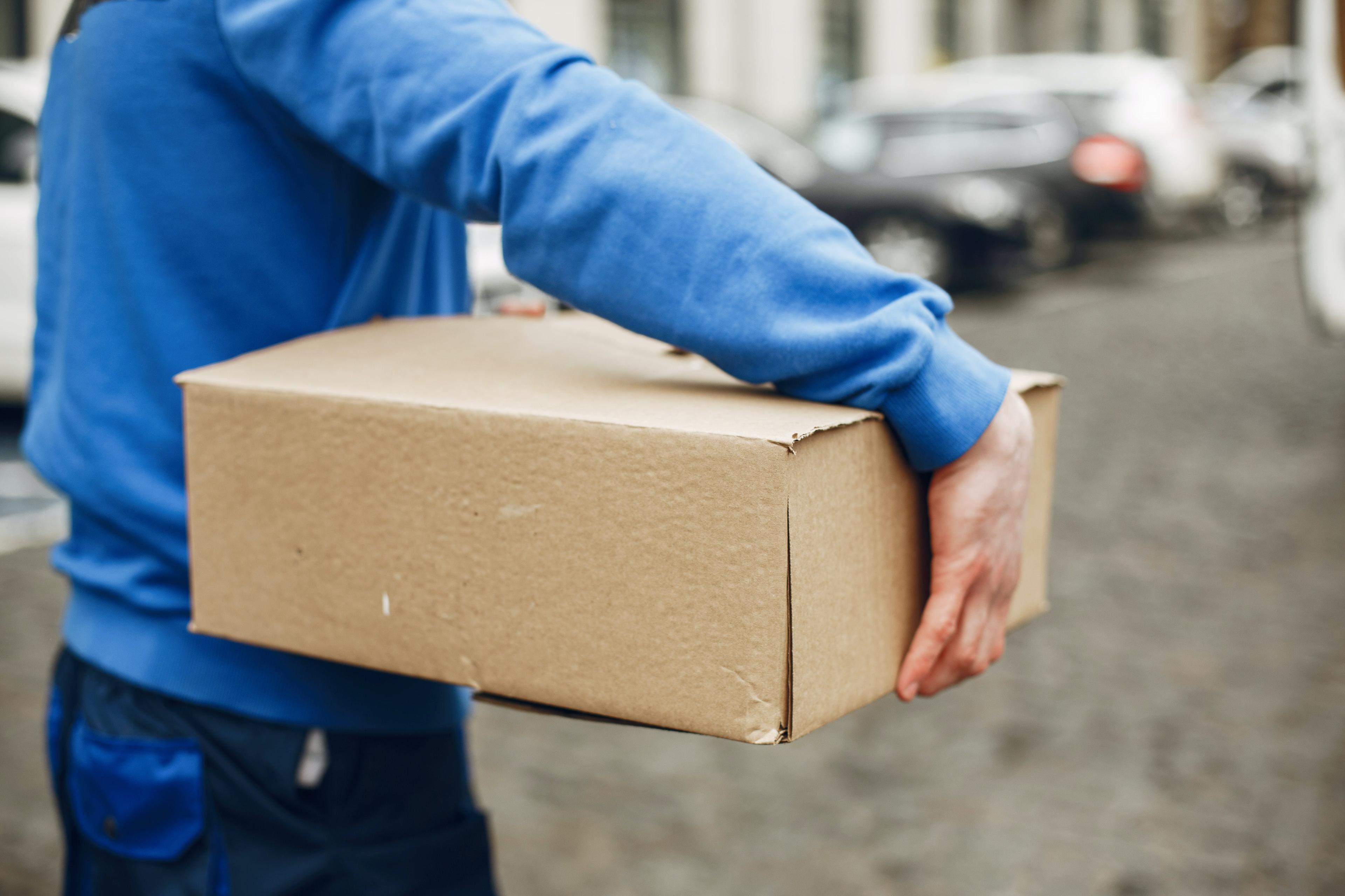 Ein Paketbote mit einem blauen Pullover trägt ein Paket.