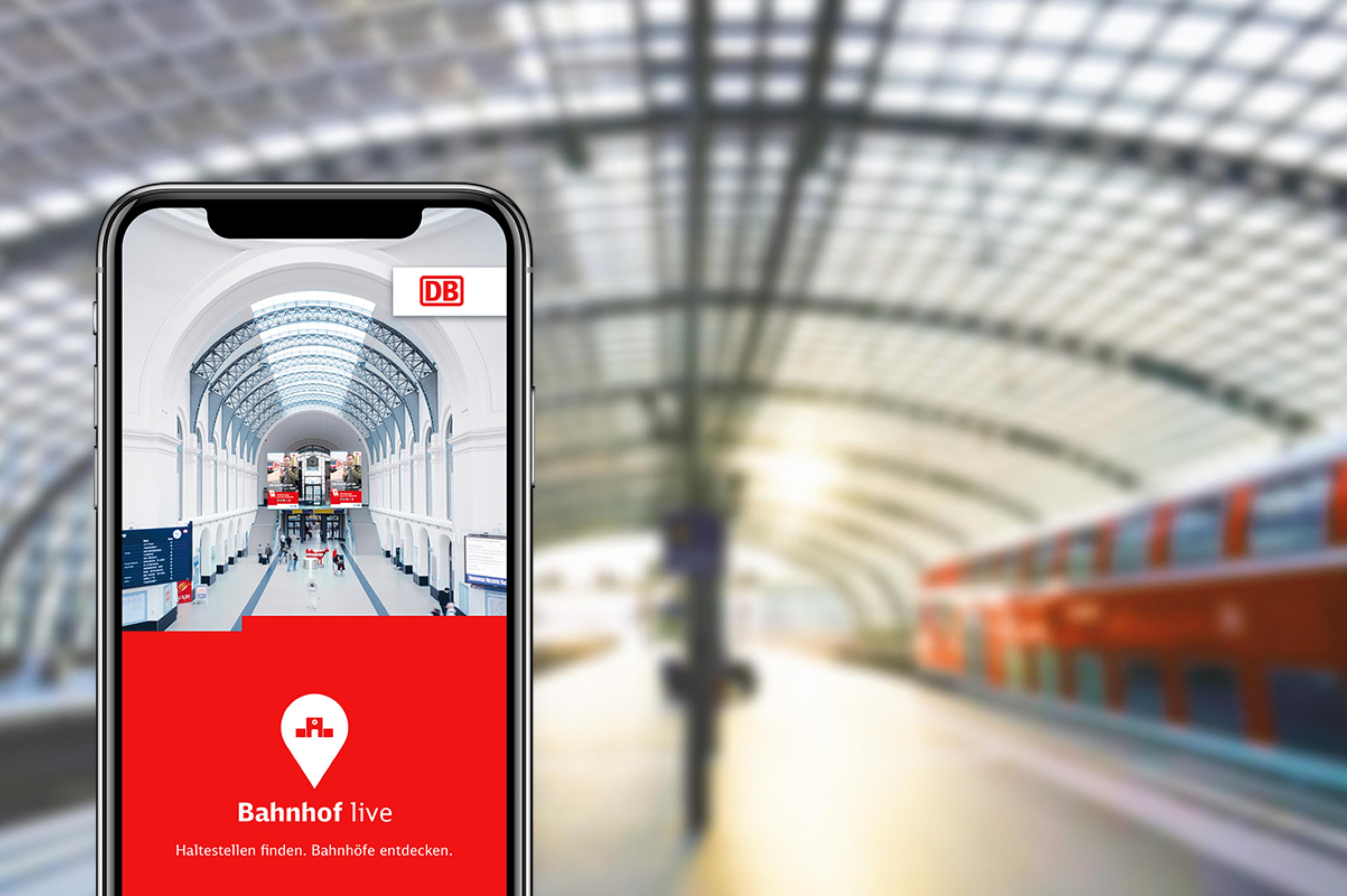 In the foreground of a platform with a stopping regional train, a smartphone with the DB Bahnhof live app is shown.