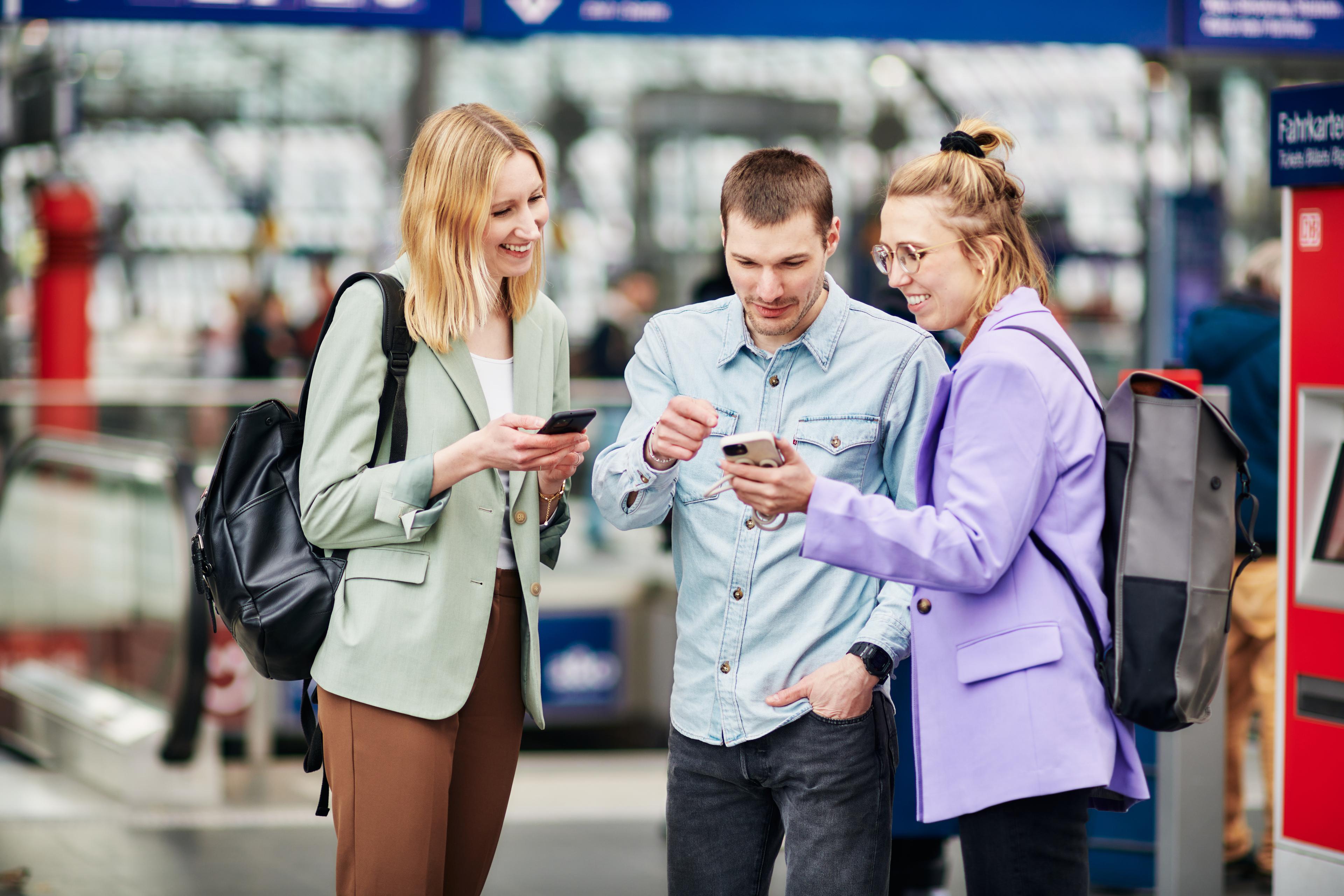 Menschen stehen am Bahnsteig und nutzen ihre Smartphones.