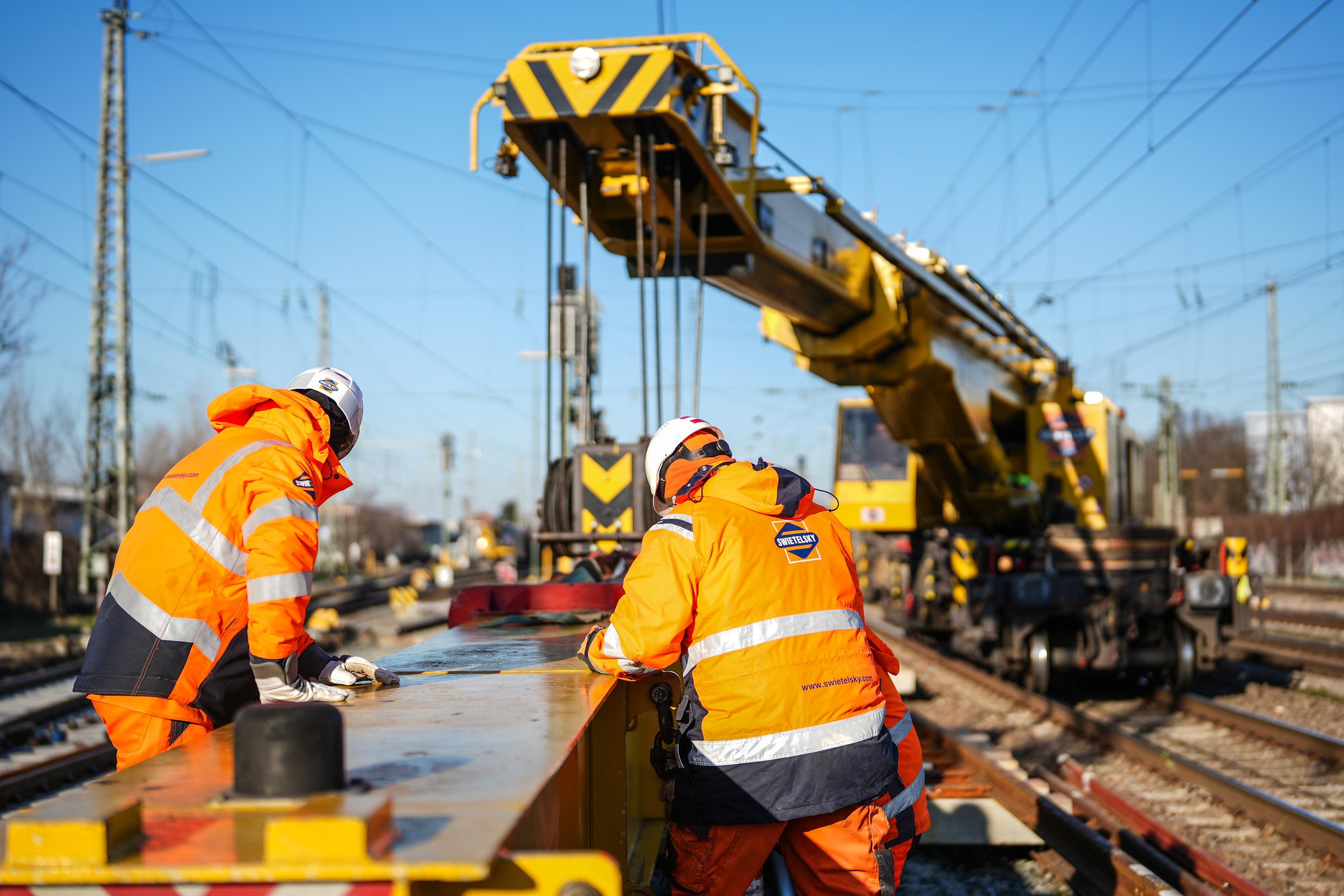 Two construction workers are working on a track.