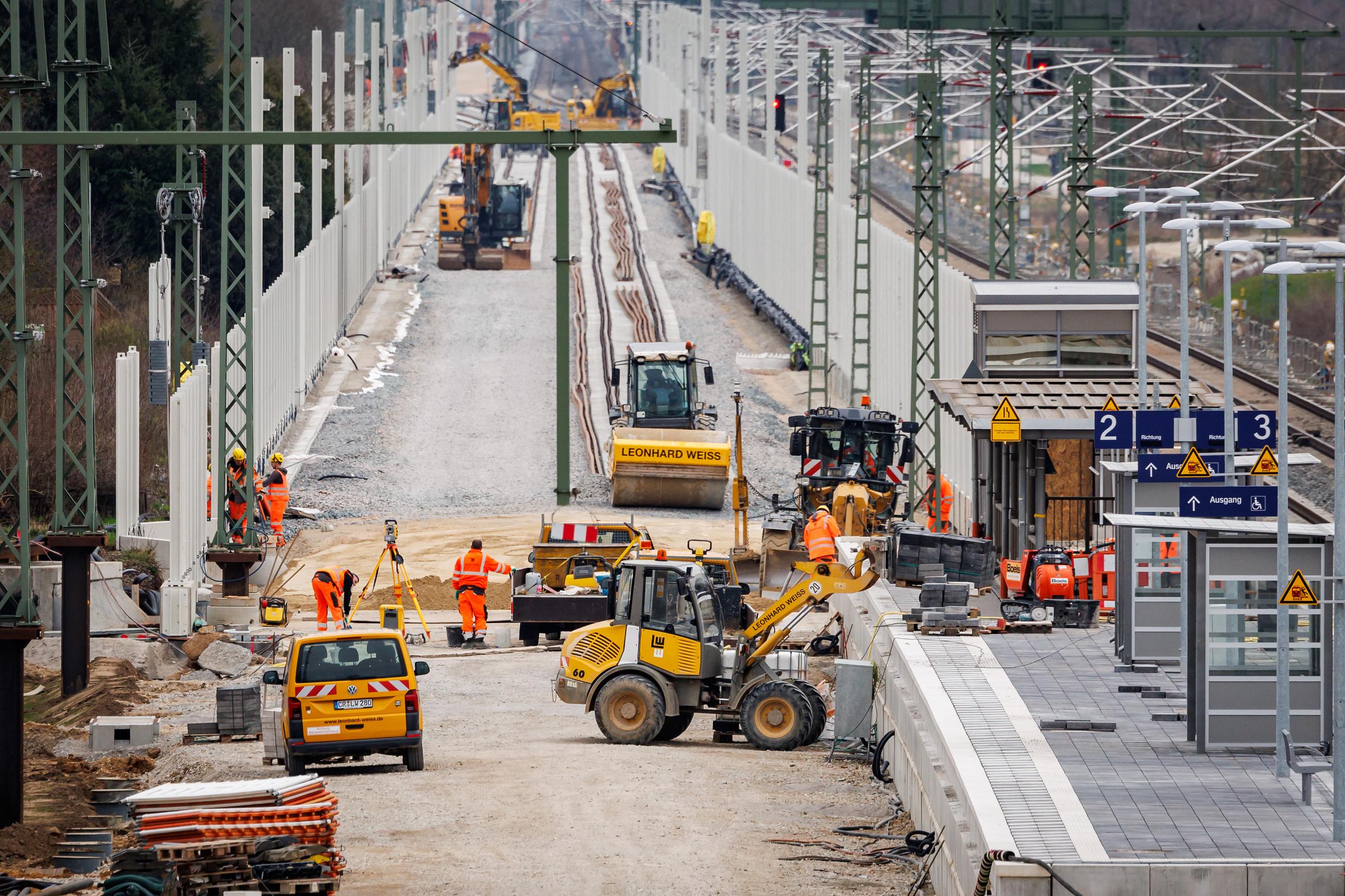 Several construction site vehicles and construction workers are working on a railway platform.