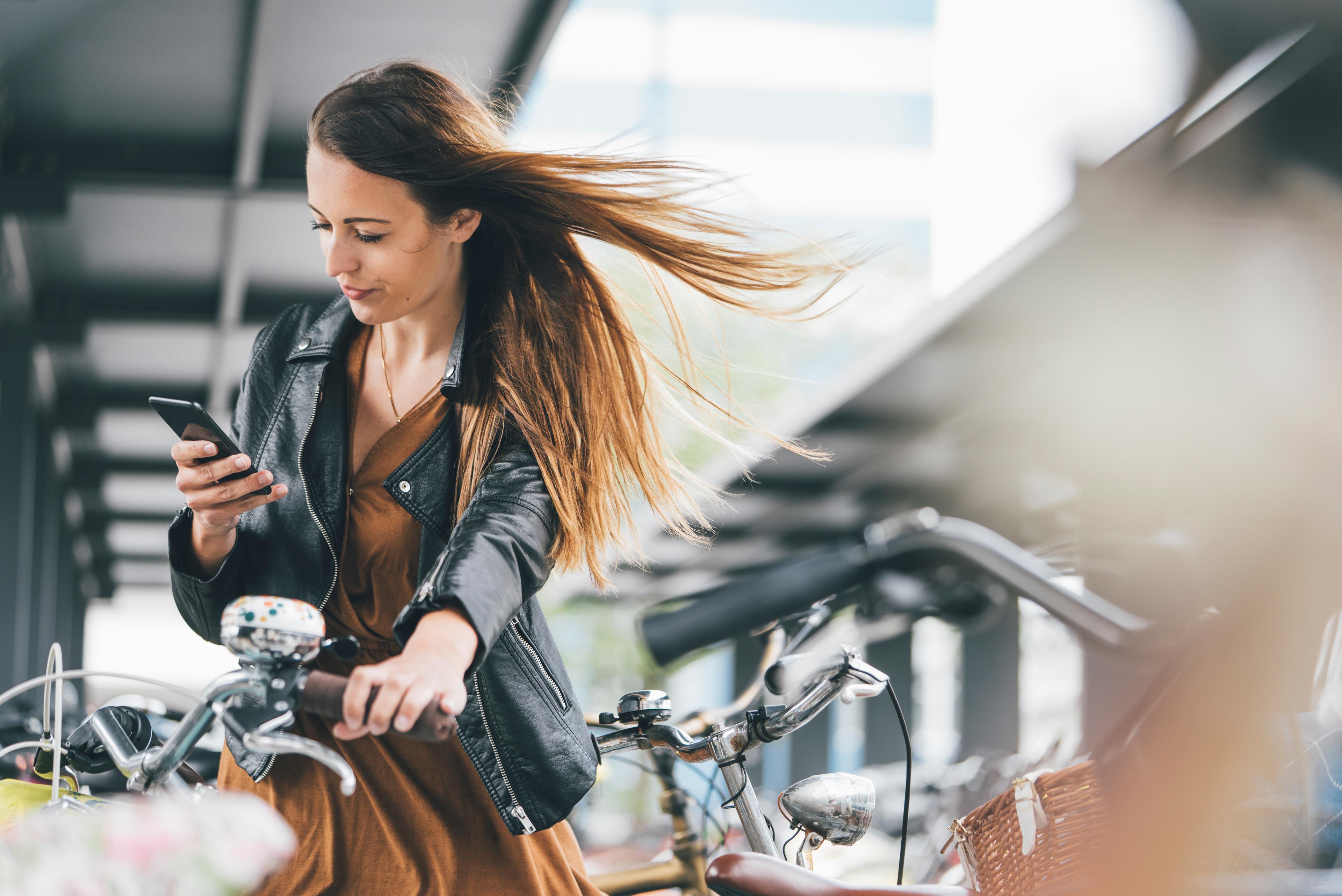 Eine junge Frau mit Fahrrad benutzt ein Smartphone in der Stadt.