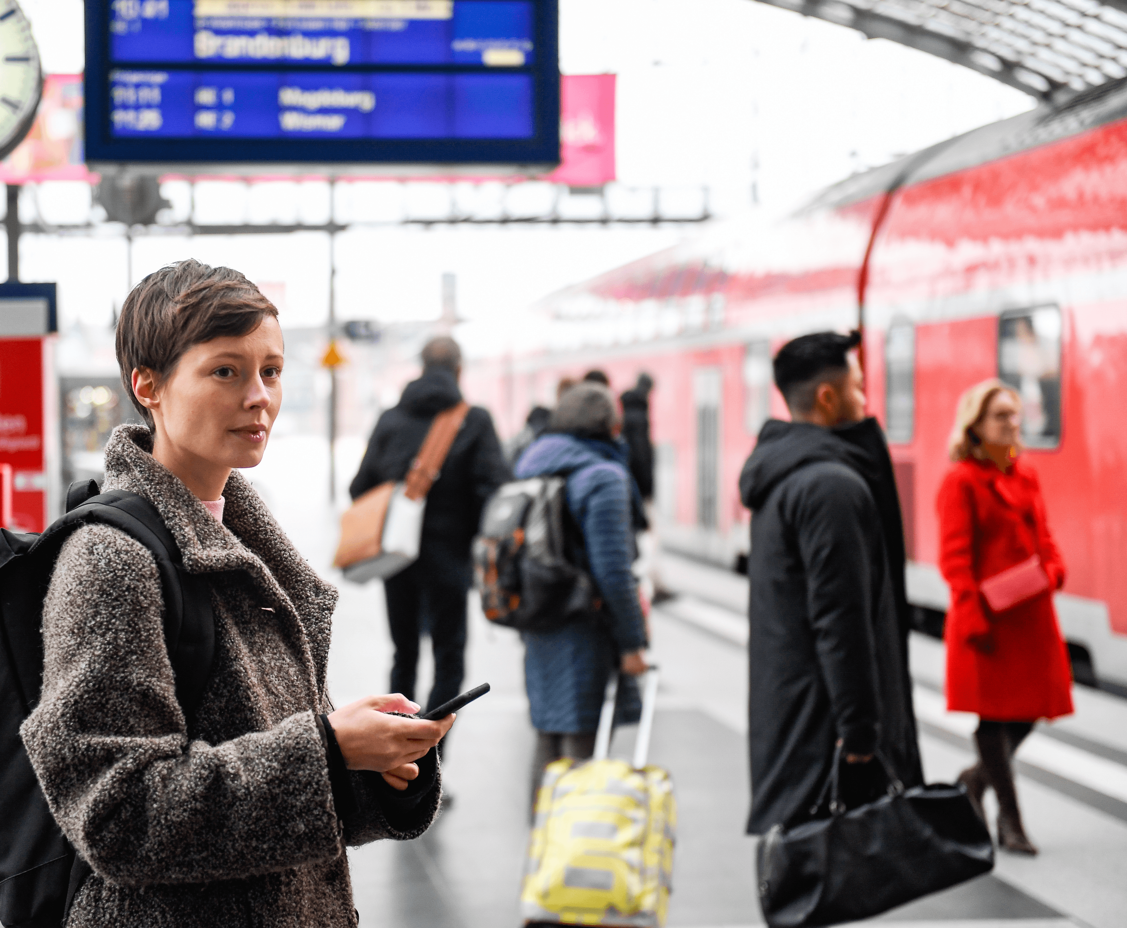 A woman on the platform with a smartphone looking at a train arriving.